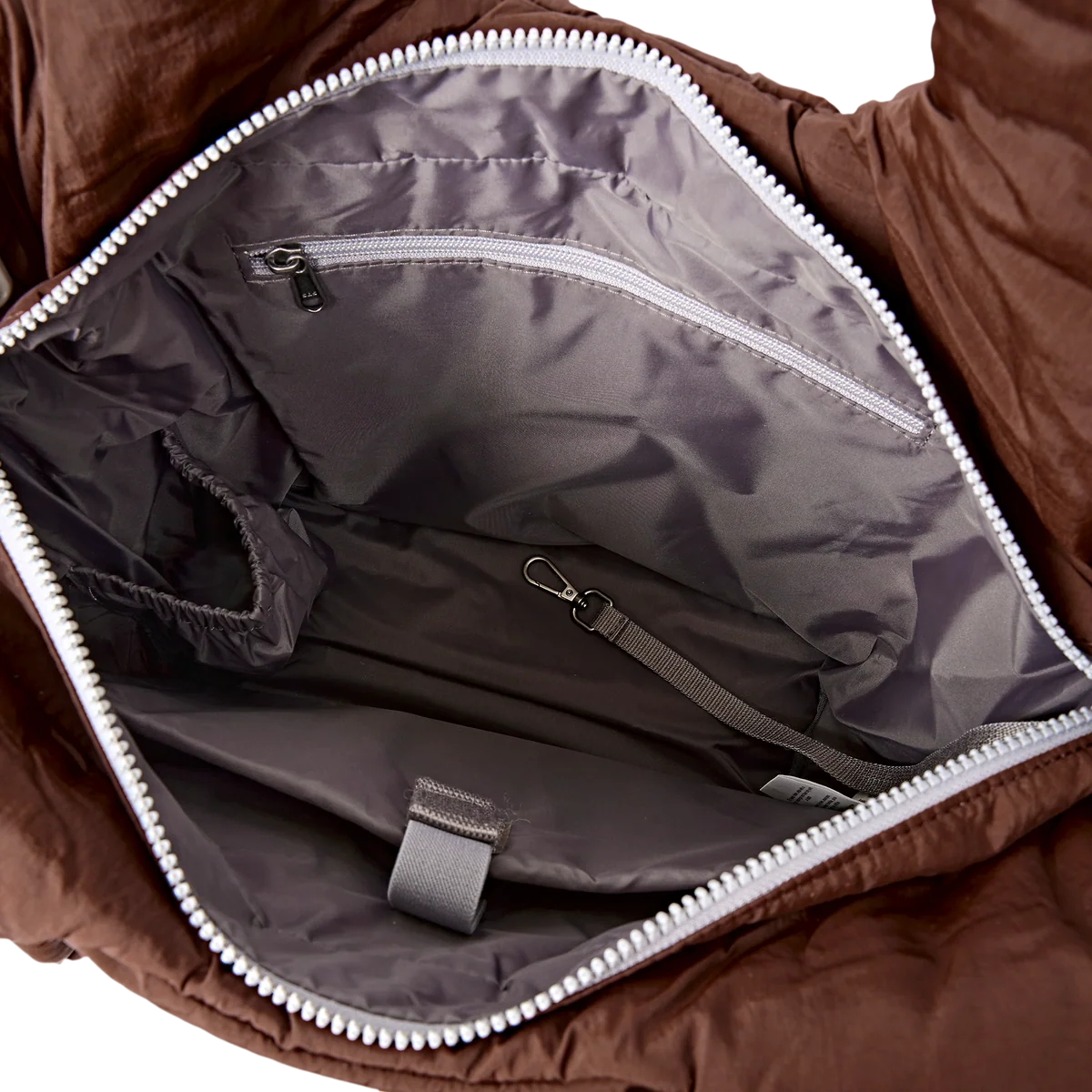 Close-up of the interior of a brown puffer bag, showing a gray nylon lining with multiple zippered compartments, a strap, and a loop tab.
