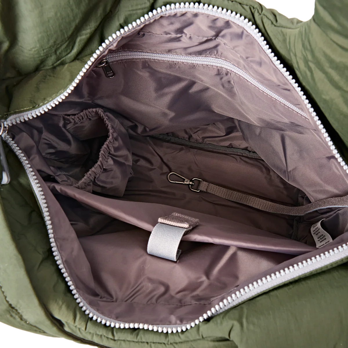 Close-up of the interior of an olive green puffer bag, showing a spacious taupe-brown nylon lining with silver zippers, a storage pocket, elastic pocket, and a hook-and-loop strap.