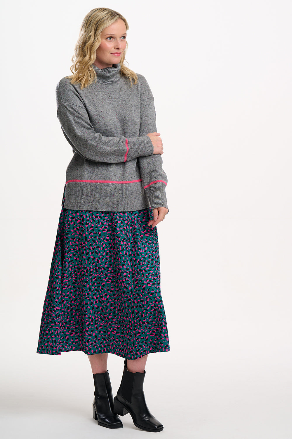 Woman wearing a gray sweater with pink trim and a patterned skirt on a white background