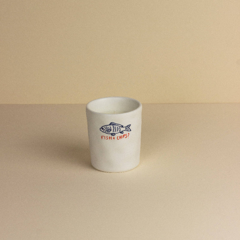 White ceramic candle with fish and chips design on a beige background
