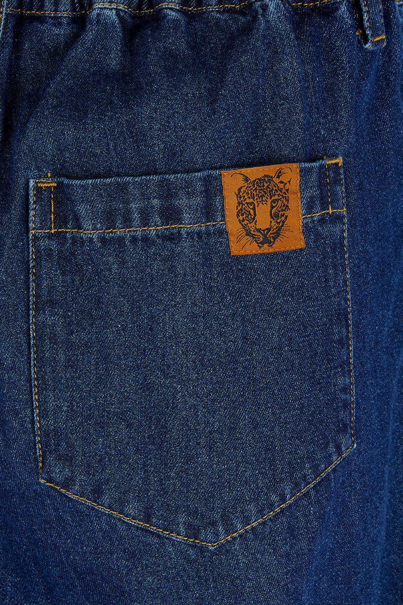 Close-up of the back pocket of dark blue denim jeans with contrast yellow stitching and a small tan leather patch featuring a black tiger face logo.