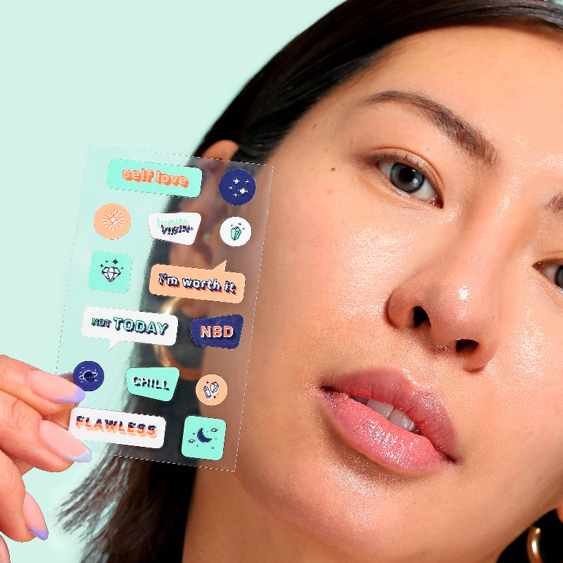 Person holding a sheet of motivational stickers near their face against a light blue background