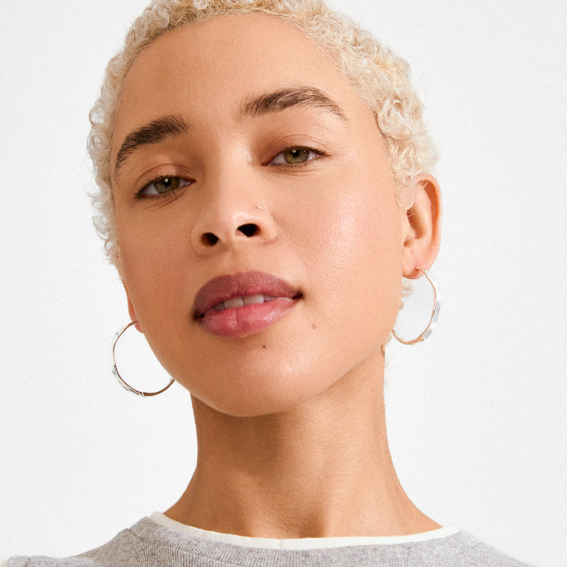 Close-up of a person with short blonde hair wearing hoop earrings on a white background