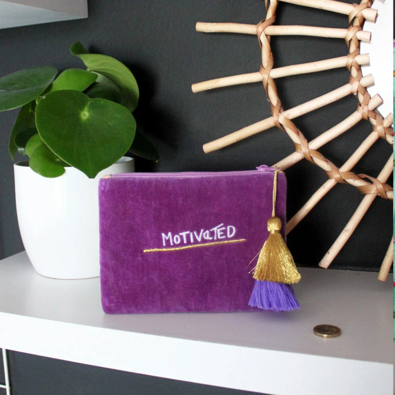 Purple pouch with 'Motivated' text and gold tassel on a surface with decorative elements.