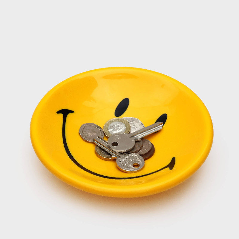 Yellow plate with a smiley face design filled with coins on a white background