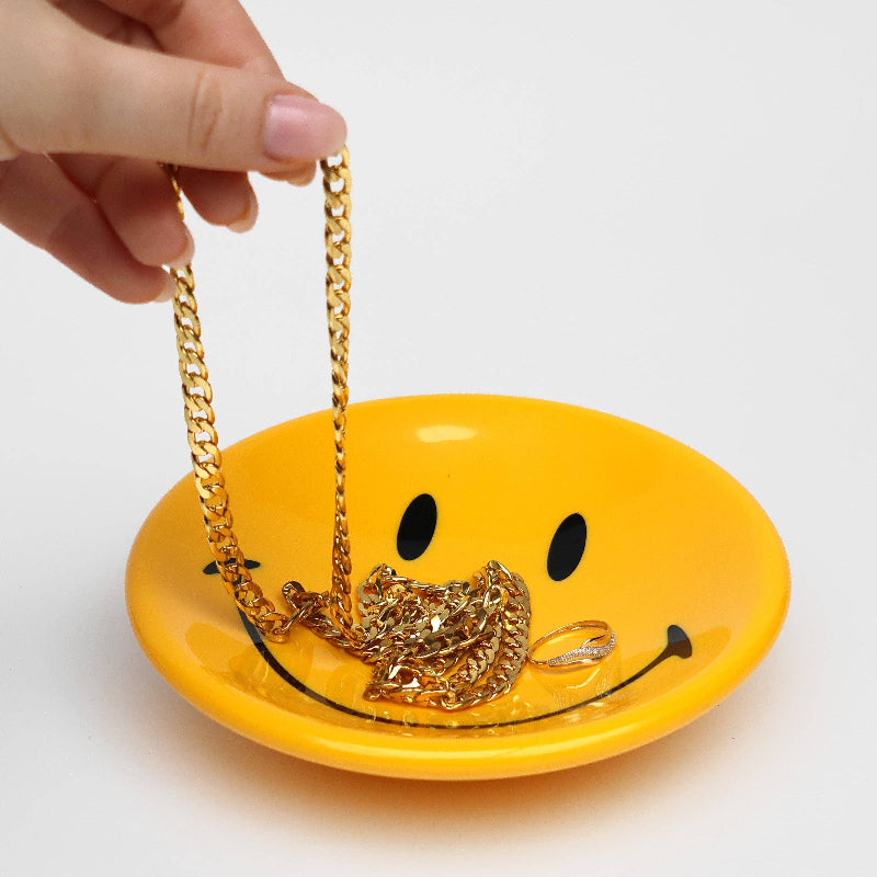 Yellow smiley face jewelry dish with gold chain on a white background