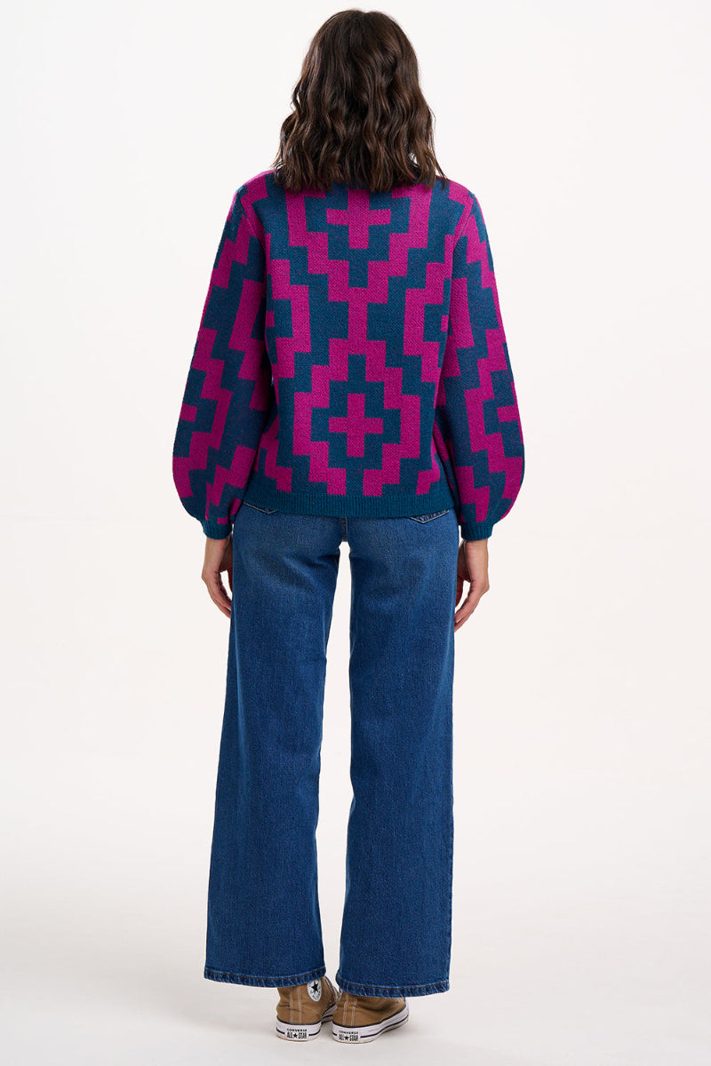 Person wearing a Sugarhill Essie Jumper Teal/Pink Diamondand blue jeans on a white background