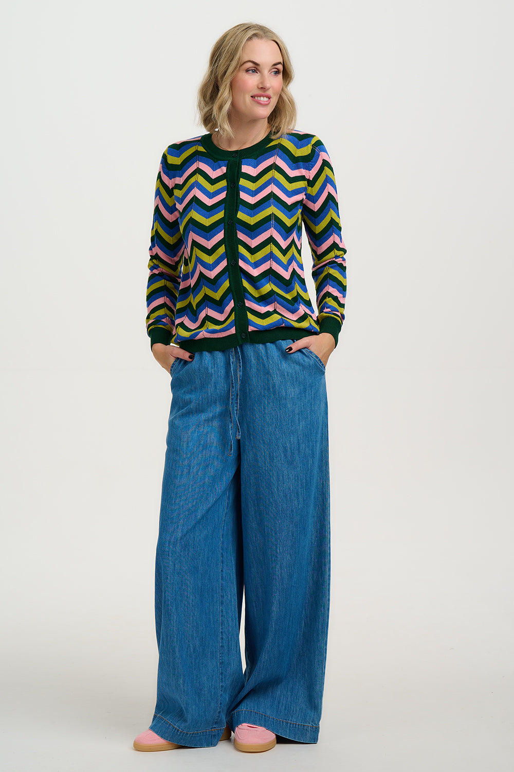 Woman wearing a Sugarhill Rochelle Cardigan colorful chevron-patterned sweater and blue jeans on a white background