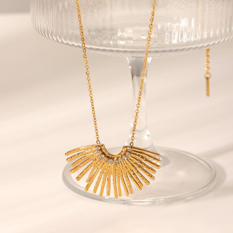 Gold necklace with a sunburst design on a clear stand