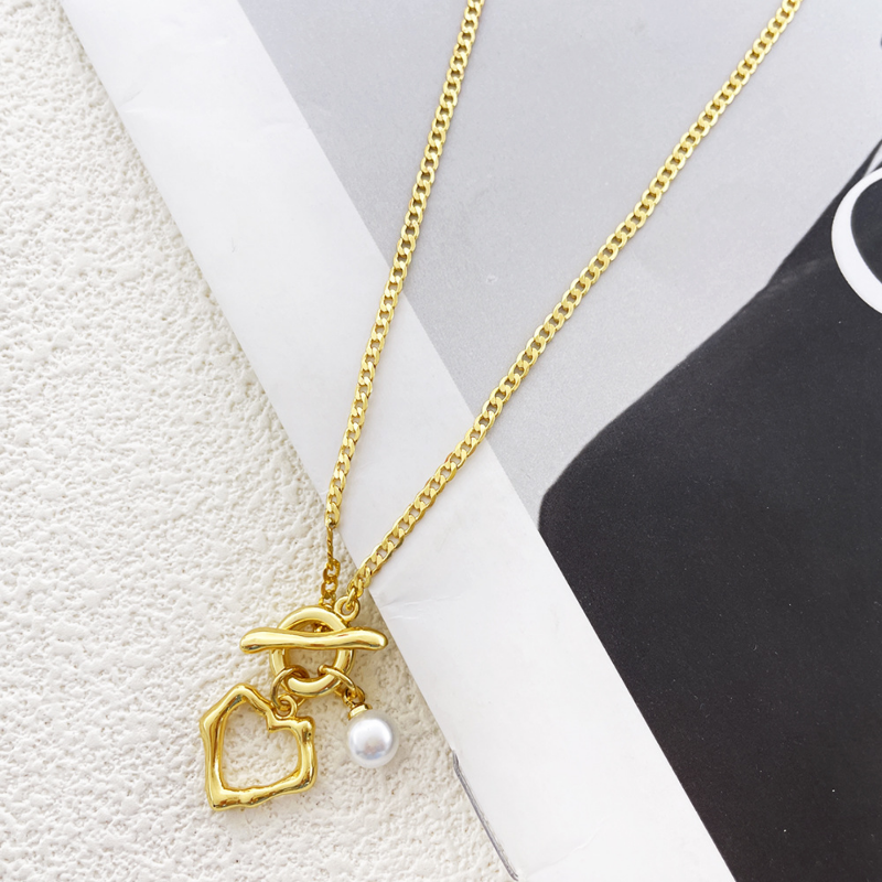 Gold necklace with a heart-shaped pendant and pearl on a white and black background