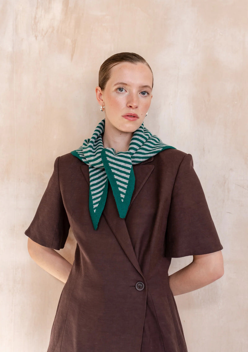 Woman wearing a brown coat and TBCO green and white striped scarf against a beige background
