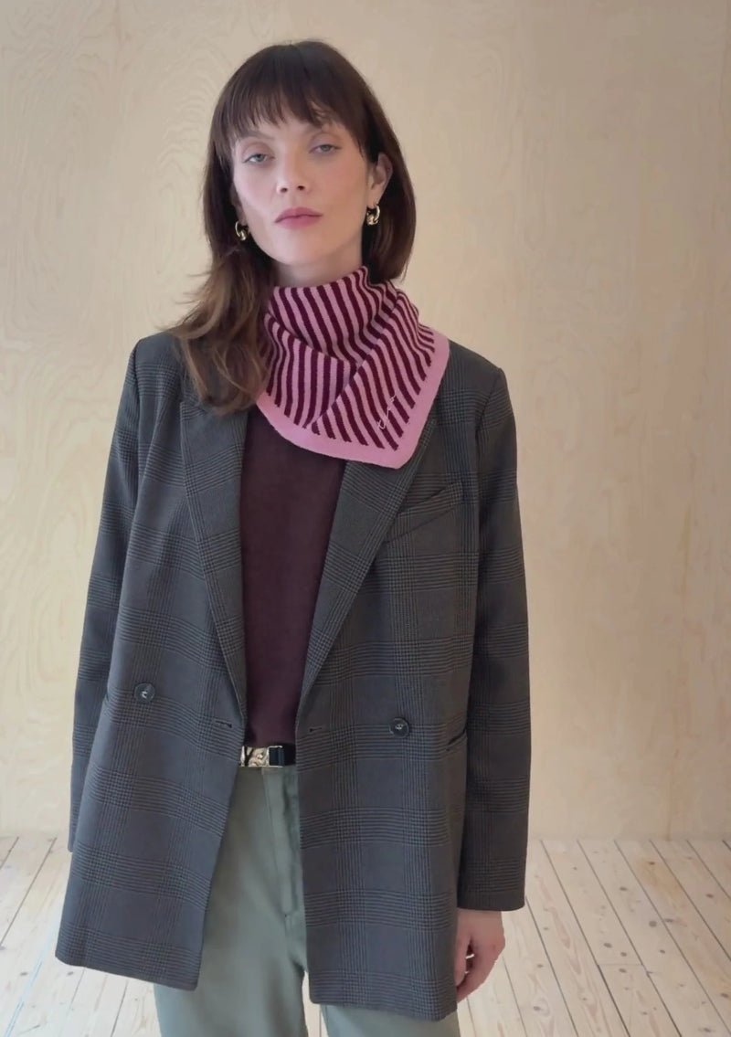 Woman wearing a grey coat and TBCO pink striped scarf against a plain background