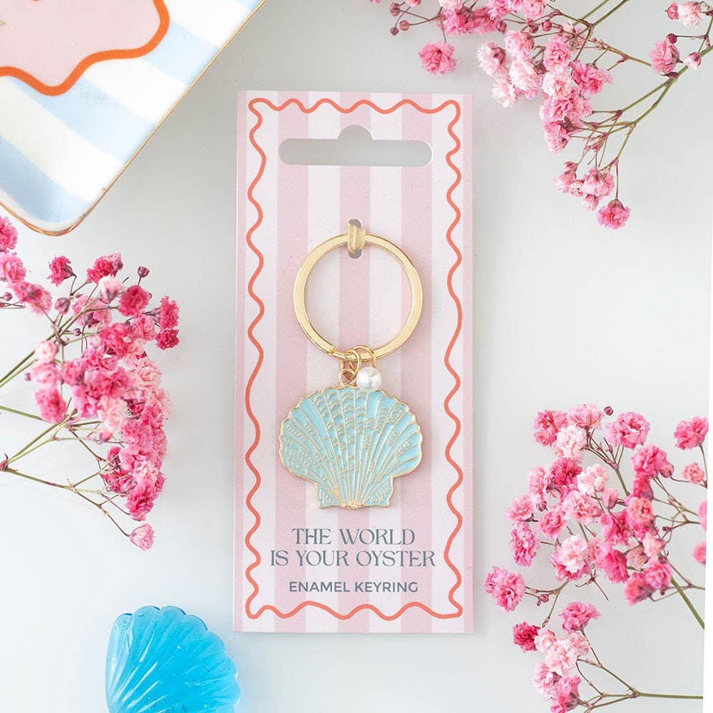 Seashell-shaped enamel keyring on a pink and white striped card with flowers around