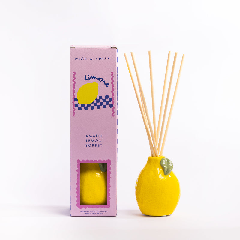 Yellow diffuser bottle with wooden sticks and pink packaging on a white background
