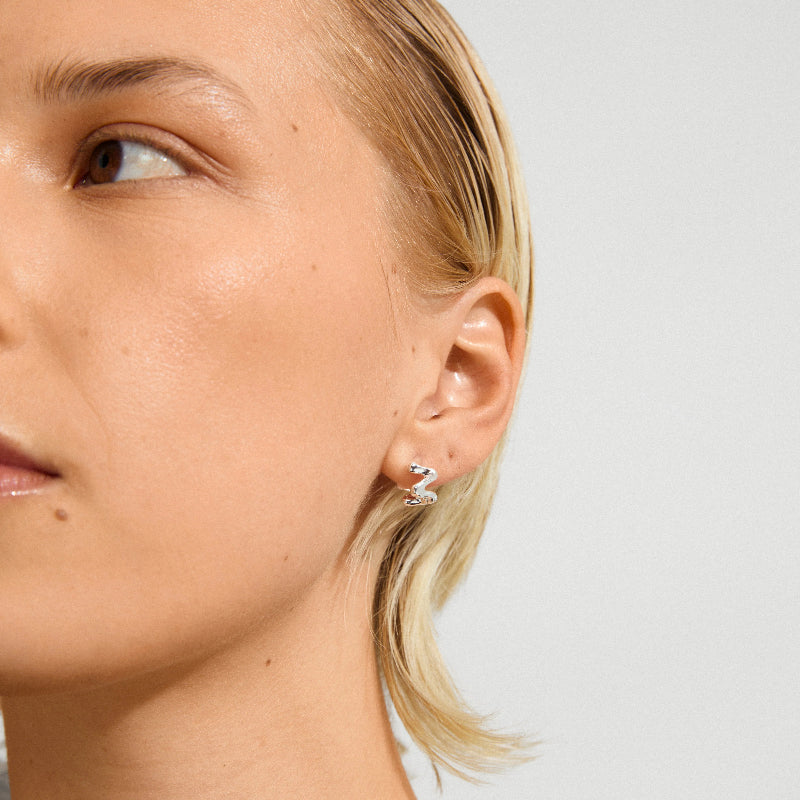 close up of silver wavy earrings on model against white background