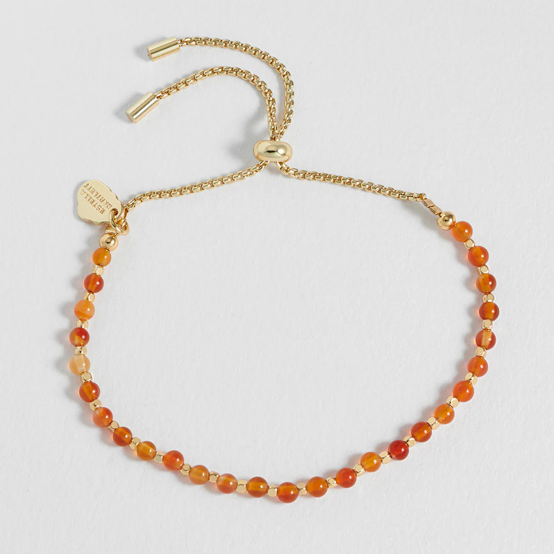 Gold bracelet with orange beads on a light gray background