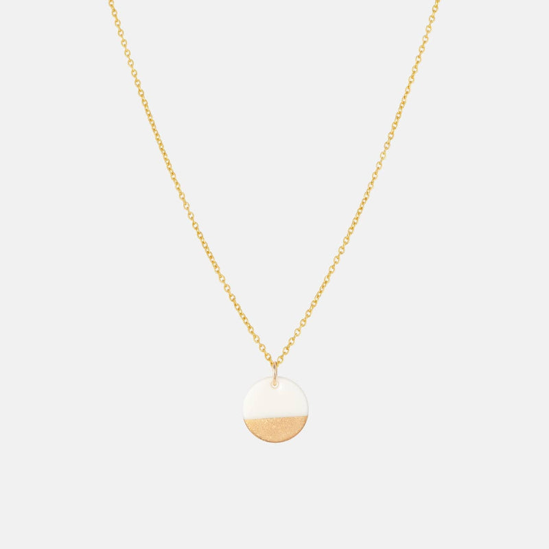 Gold necklace with a round pendant on a light gray background