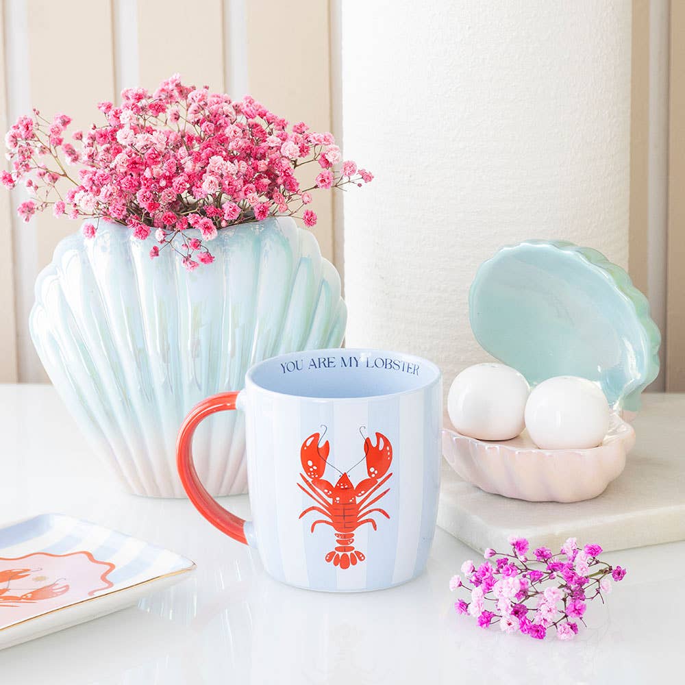 Mug with a lobster design on a table with flowers and decorative items.