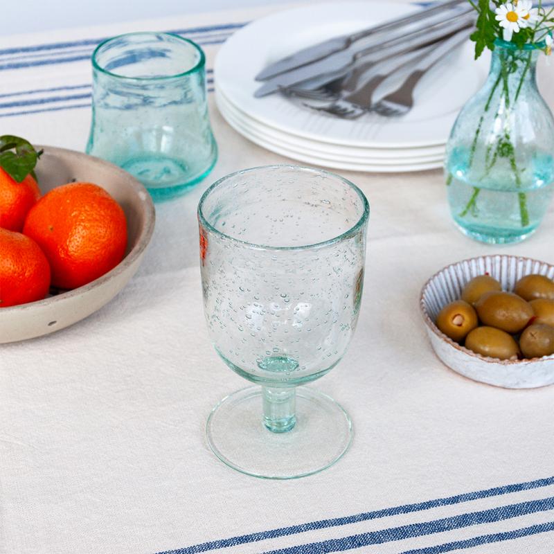 Clear glass goblet on a table with oranges, olives, and cutlery.