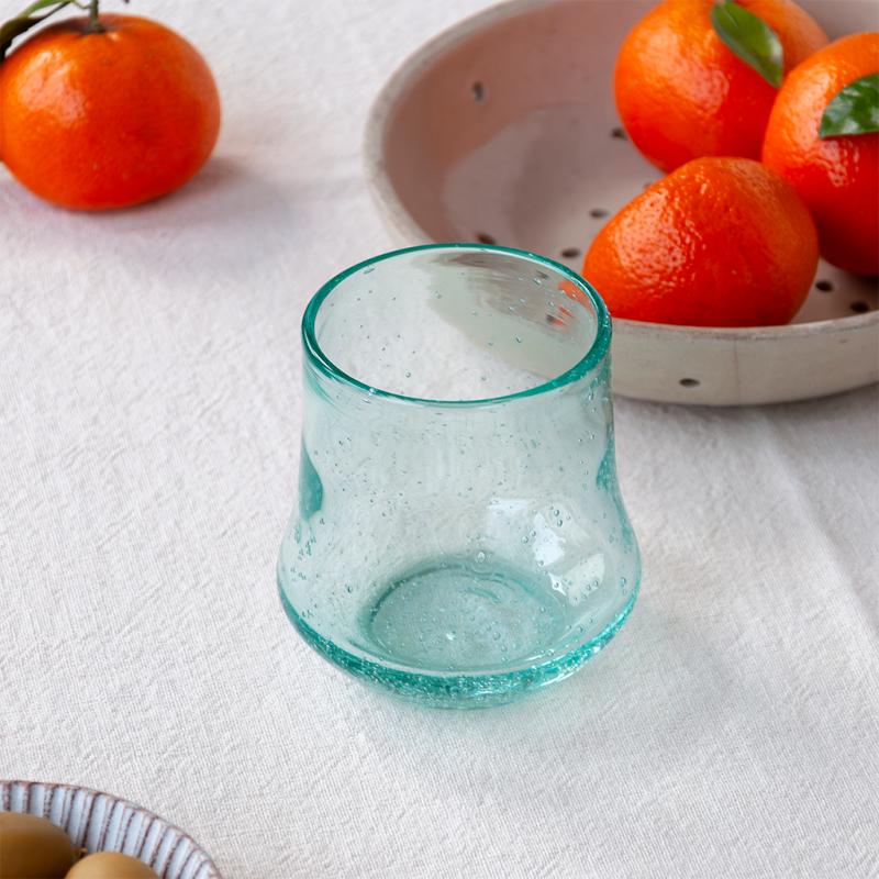 Turquoise glass tumbler on a white surface with mandarin oranges in the background