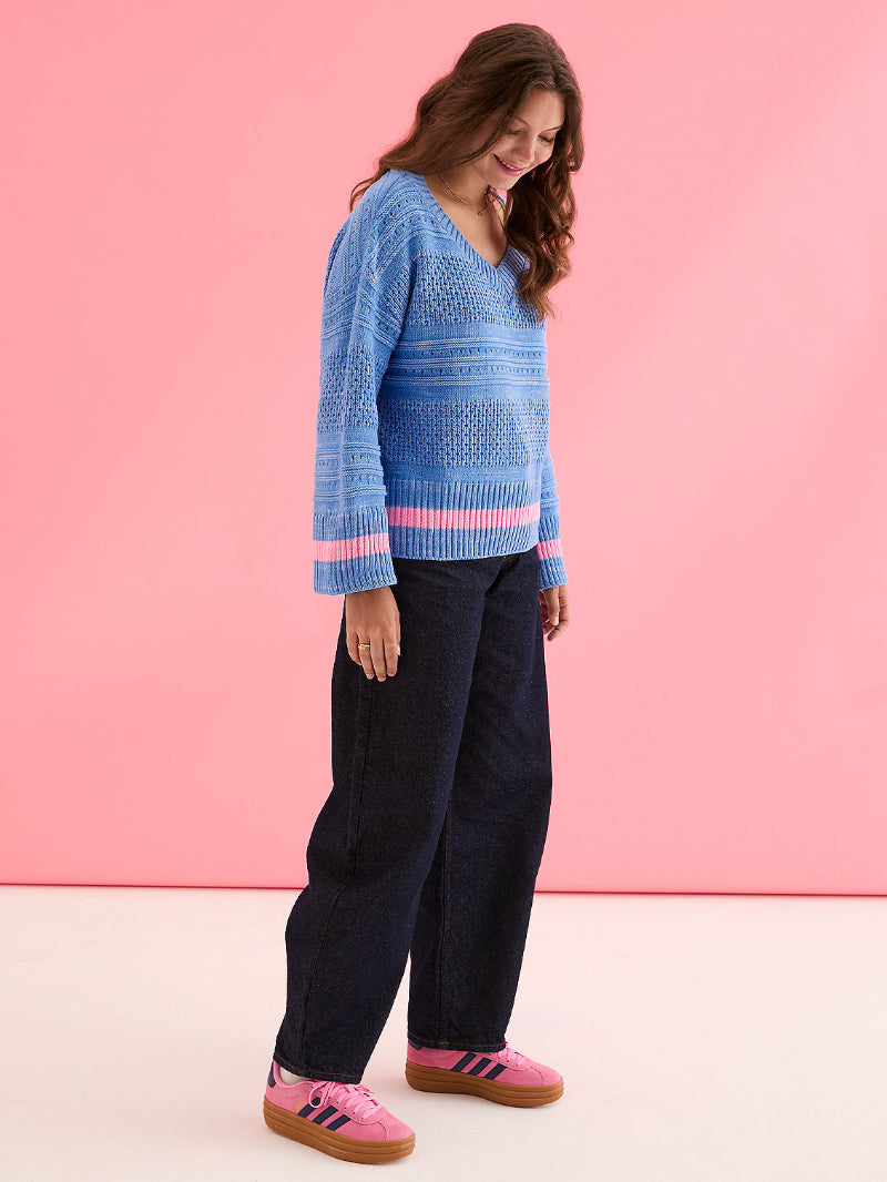 Woman wearing Cara & The sky JudithJumper Blue_Front a blue patterned sweater with pink accents against a pink background
