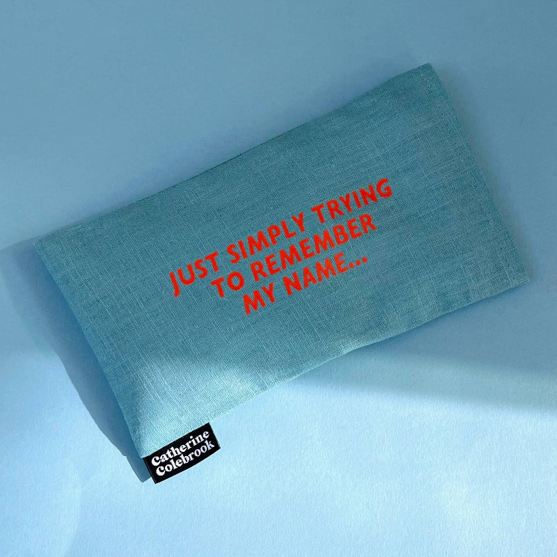 Blue notebook with red text 'JUST SIMPLY TRYING TO REMEMBER MY NAME...' on a light blue background