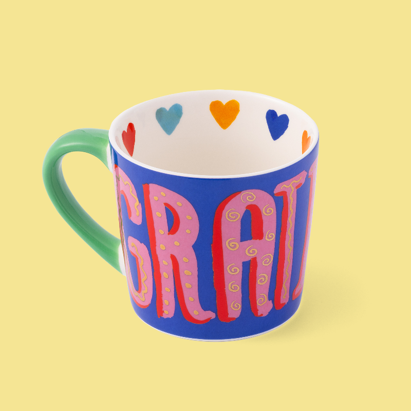 Colourful mug with 'GRATitude' text and heart shapes on a yellow background