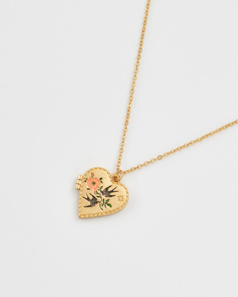 Fable Swallow Heart Locket Chain Necklace. Gold heart-shaped necklace with floral design on a light grey background