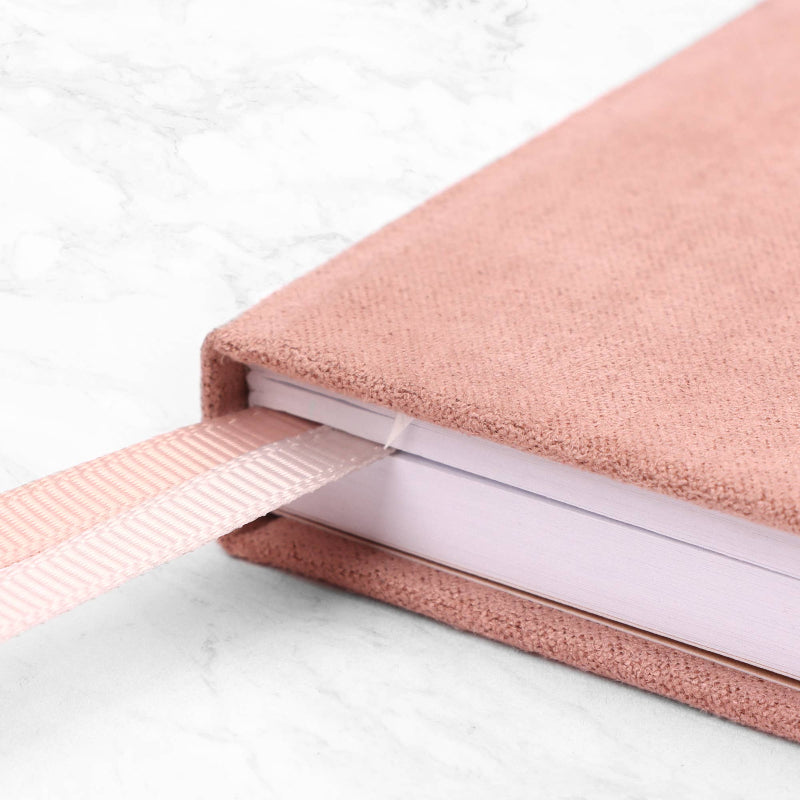 Close-up of a pink fabric-bound book on a marble surface