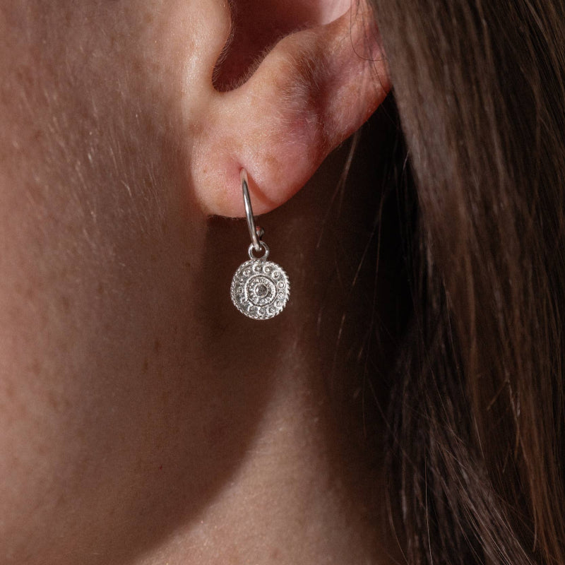 Close-up of an ear wearing a silver earring with a circular design.