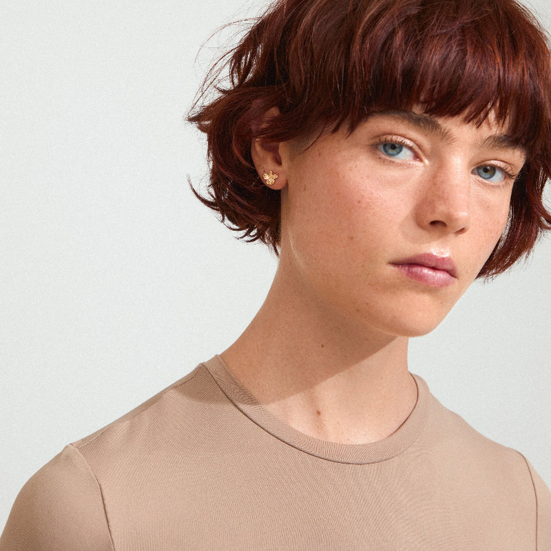 Person with short red hair wearing a beige shirt against a light background