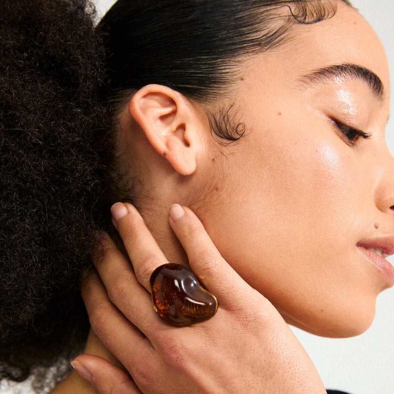 Close-up of a person wearing a amber-colored ring on their finger.
