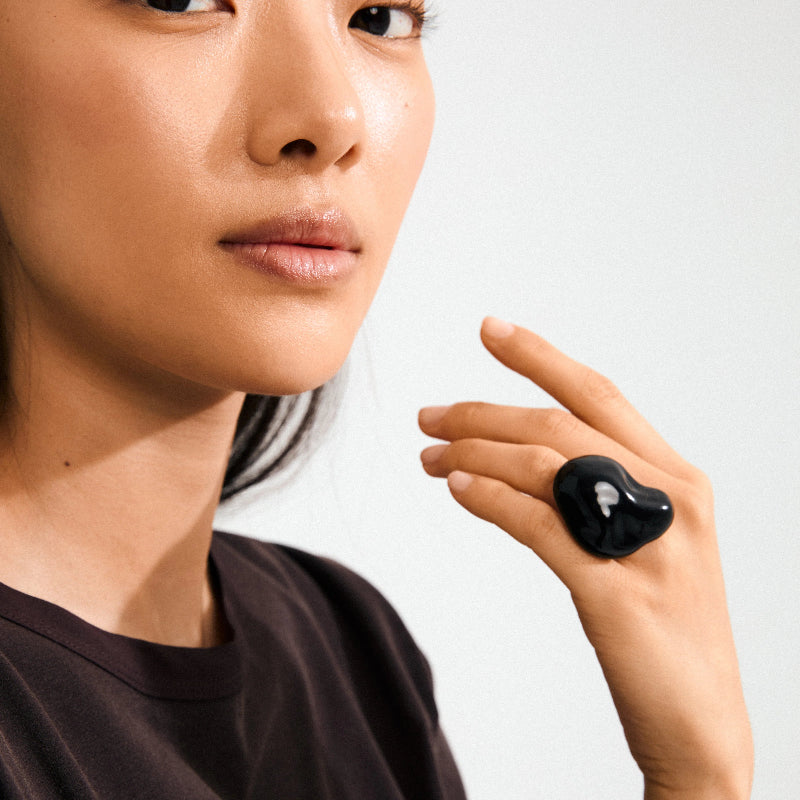 Person wearing a black heart-shaped earring on a plain background