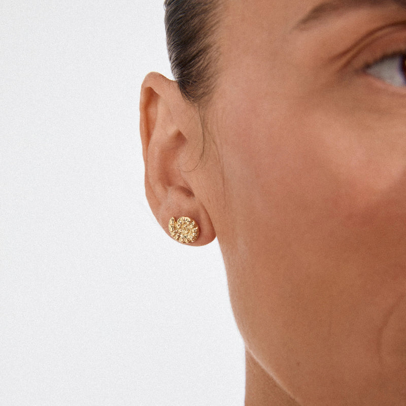 Close-up of a person wearing a Pilgrim Haze Earrings Gold Plated a light background