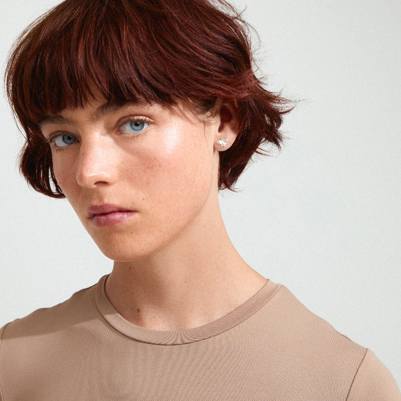 Woman with short red hair wearing a beige top against a plain background
