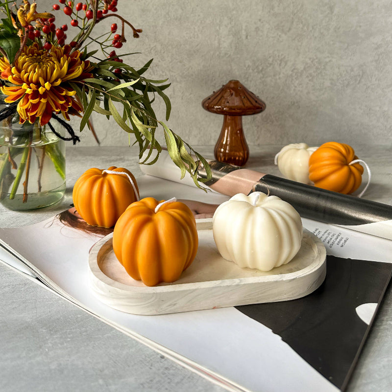 Decorative setting with pumpkins, flowers, and a mushroom on a gray surface.