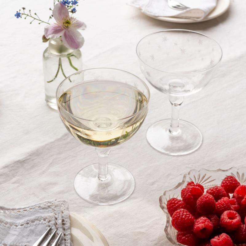 Coupe glass with white wine, raspberries, and flowers on a light surface