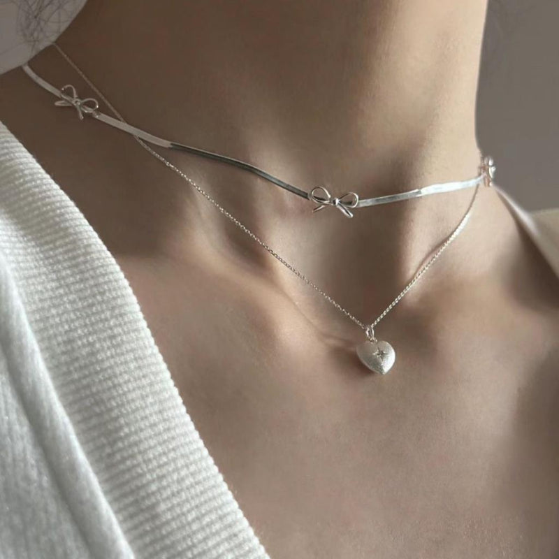 Silver necklaces with bow and heart pendants on a neutral background