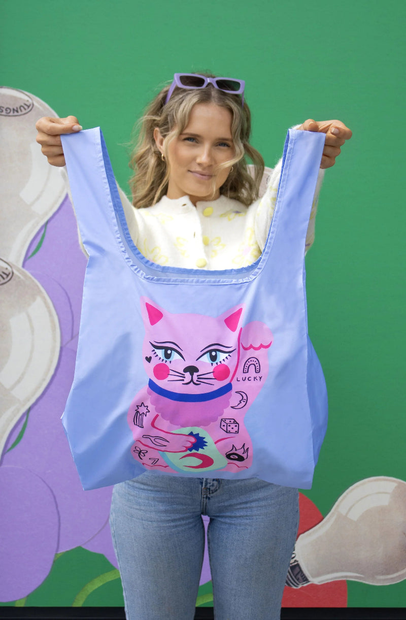 Person holding a blue tote bag with a pink cat design against a colorful background