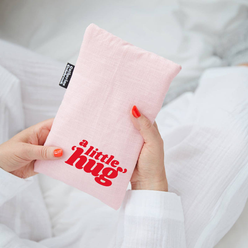 Pink pillow with 'a little hug' text held by a person wearing a white robe.