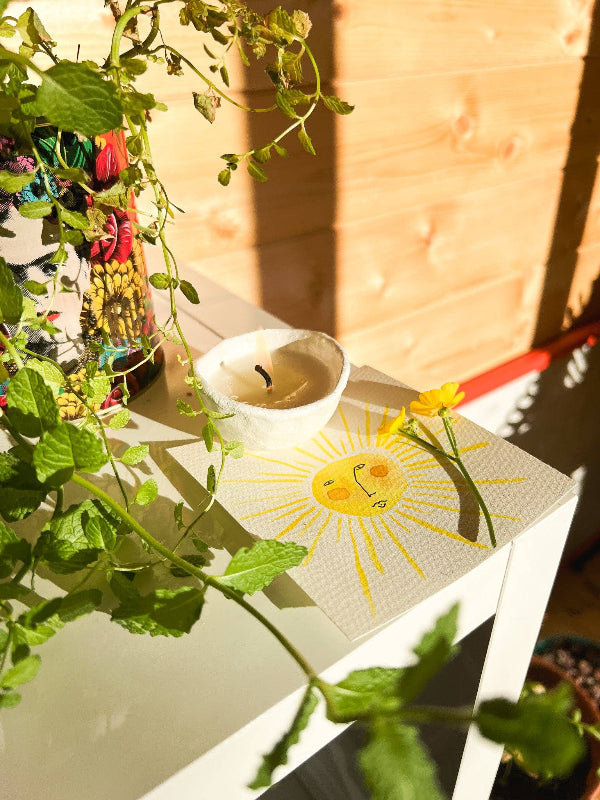 Candle with a sun design on a table surrounded by plants