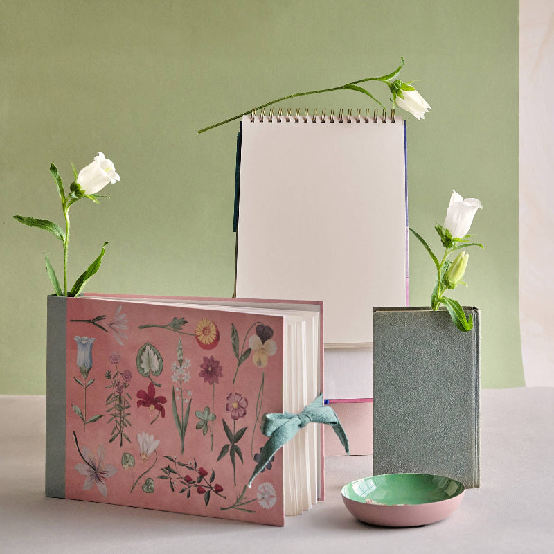 Three books with floral designs and white flowers on a light green background