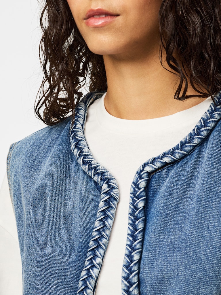 Close-up of a person wearing a blue denim vest with a white shirt underneath.