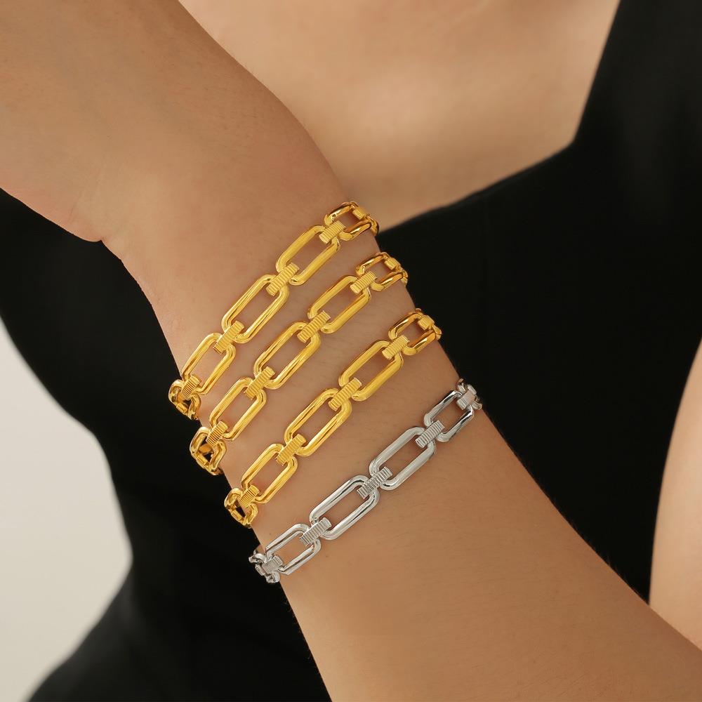 Gold and silver chain bracelets on a wrist against a neutral background