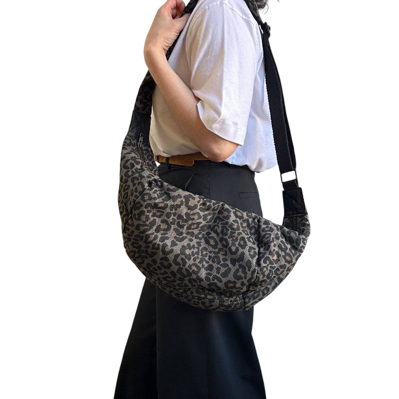 A person wearing a white short-sleeve shirt and dark skirt carries a large slouchy shoulder bag with a gray and black leopard print pattern against a plain white background.