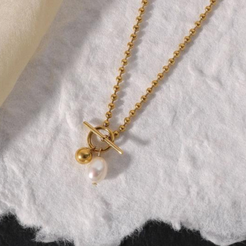 Gold necklace with a pearl pendant on a textured white surface