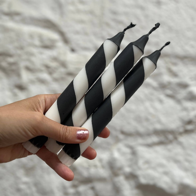 Hand holding black and white striped candles against a textured gray background