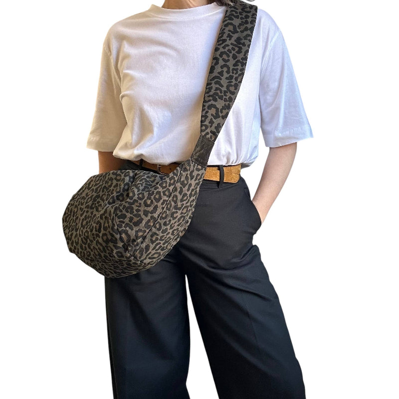 A person wearing a white t-shirt and dark wide-leg pants carries a leopard-print shoulder bag across their torso against a plain white background.