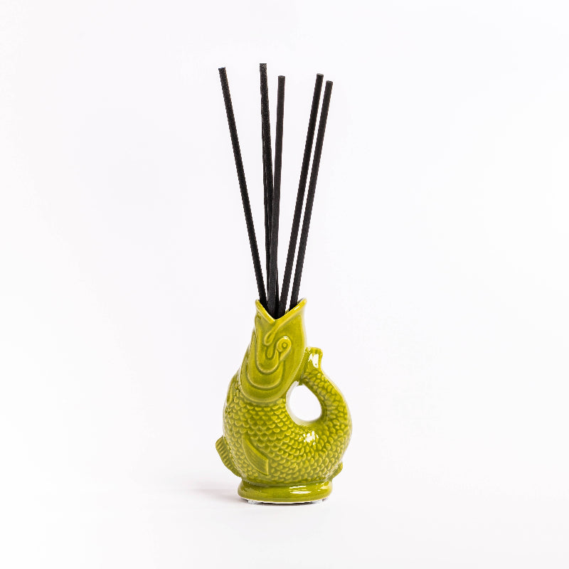 Green ceramic diffuser with black sticks on a white surface with a blurred background