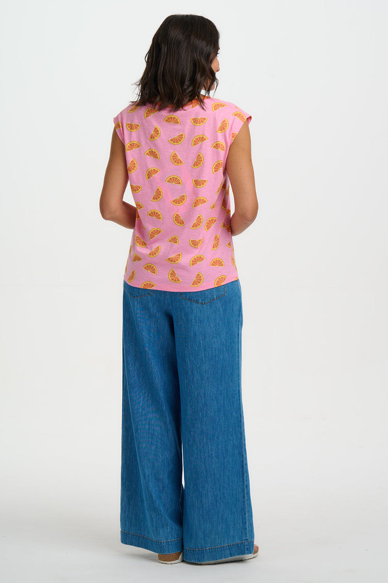Person wearing a pink sleeveless top with fruit pattern and blue jeans on a white background